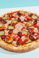Italian pizza with sausage, jalapeno, ham and paprika on coloured background. Spicy pizza with jalapeno in minimal style on blue and orange color. American pizza delivery concept with color backdrop.