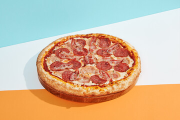 Italian pizza with salami, ham, bacon, pepperoni on coloured background. Meat pizza with sausage and bacon in minimal style on blue, orange color. American pizza delivery concept with color backdrop.