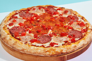 Italian pizza with salami, ham, pepperoni and paprika on coloured background. Meat pizza with salami and pepperoni in minimal style on blue color. American pizza delivery concept with color backdrop.