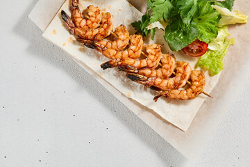 Grilled shrimps with sauce on concrete background. Aesthetic composition with prawn skewer and fresh herbs. Shrimps on grill in summer menu. Seafood skewer in minimal style.