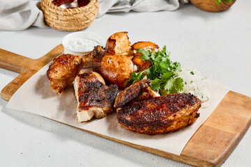 Roasted chicken with spices and herbs on wooden plate. Traditional caucasian food - chicken tabaka. Grilled chicken with bread and sauce on concrete background.