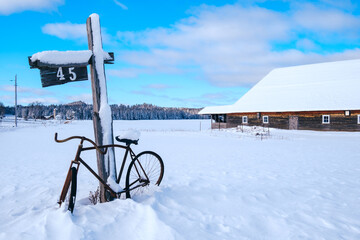 View on an old bicycle, a mail box, a street sign and an old barn, all covered by the snow on a...