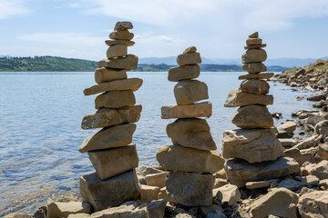 Fototapeta na wymiar Rock cairn the art of stone balancing on a stone near a blue water flowing lake. Sunny day on the lake. A mood of calm and harmony with nature.