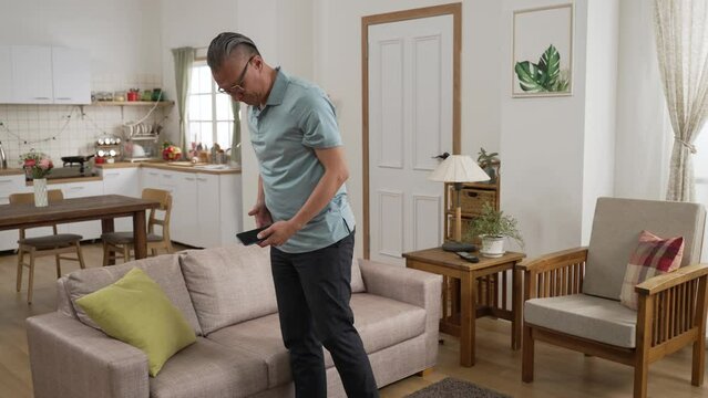 fast forward with full length asian retired man looking everywhere for mobile phone in the living room at home during the day. he found it behind the pillow on sofa