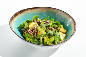 Healthy pasta soba with green vegetables. Vegetarian dish - soba with zucchini, broccoli and green pea on ceramic bowl. Veggie food handmade bowl isolated on white background. Plant based bowl dining.