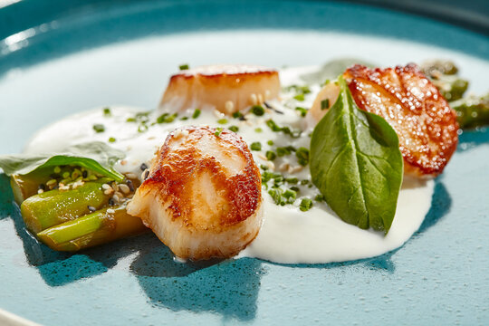Luxury dish - grilled scallops with asparagus and creamy espuma. Roasted scallop with cream sauce and asparagus on white background. Delicacy seafood in restaurant menu -  sea scallop.