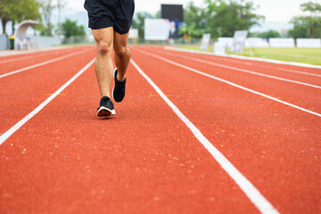 Obraz premium Close up legs Young chinese man wearing sportswear running on track at sport stadium. Fit man jogging outdoor cross the finish line. Exercise in the morning. Healthy and active lifestyle concept.