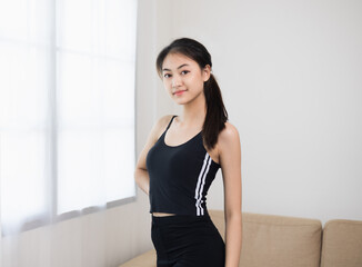 Fototapeta na wymiar Young beautiful asian woman standing pose smiling to camera. Cheerfully sporty female workout and exercise wearing sport wear at home. Charming woman fitness training and stretching in living room
