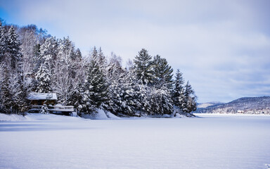 View of wooden lakehouse by a frozen near Tremblant ski resort on a cold winter day in Quebec...
