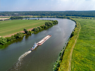 Small towboat pushes barge along calm water past fields