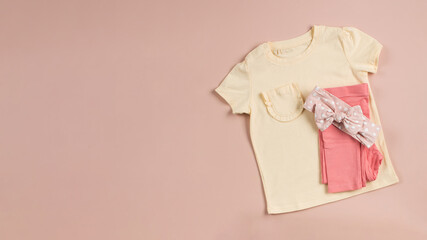  Yellow children's t-shirt and folded pink pants on a pink background. Banner. Copy space.