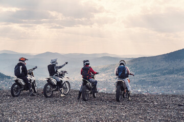 group motorcyclists traveling in mountains on dirt motorcycles, standing and enjoying mountain valley view