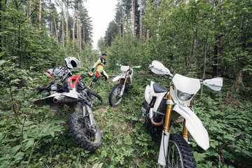 Enduro motorcyclists in deep forest at halt, checking the technical condition of motorcycles, removing logs from the path