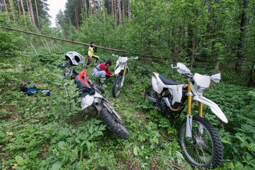 Dirt motorcycles in deep forest at halt, bikers checking the technical condition bikes, removing...