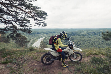 biker resting on enduro motorcycle on the edge of cliff with gorgeous view of mountain skyline