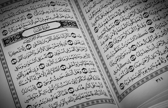 The open page of the Quran shows surah taha. Quran is an Islamic holy book for Muslims. selective focus.above prayer mat open page of Quran Black and white