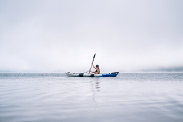 Woman kayaking on a mountain lake. Clouds and fog above the water