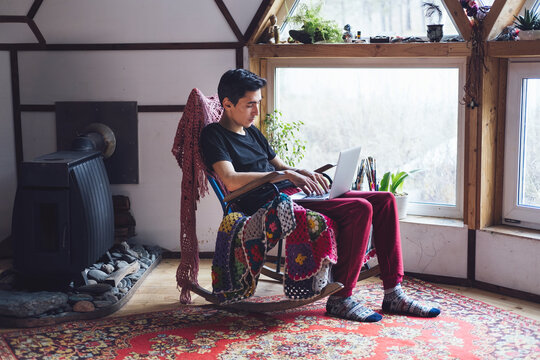 young mixed race man sitting in traditional interior in rocking chair with laptop in his hands