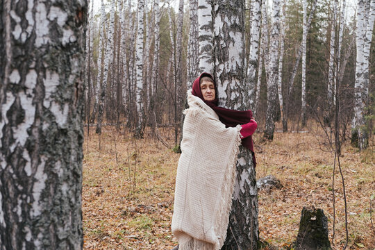 Old woman hugging birch tree in autumn forest