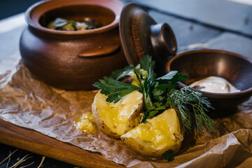 Baked potatoes on wooden board with dill and sour cream  near clay pot