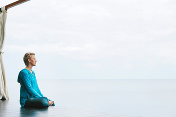 Fototapeta premium Meditation on sea shore, space for text on photo. Calm female sitting in gazebo meditating and relaxing near water skyline