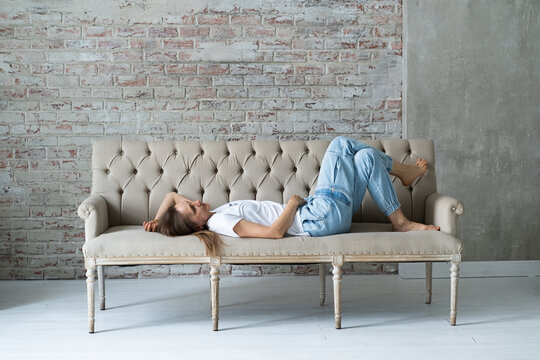 Tired woman wearing jeans lying on a sofa in spacious bright room