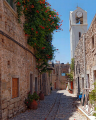 Pyrgi town, a picturesque cobblestone street with a green foliage covered house, and a church clock tower. Chios island, Greece.
