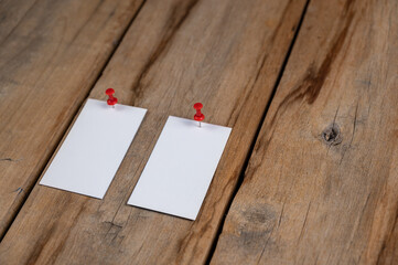 Two blank business cards against a wooden background. White paper rectangles pinned with push pins...