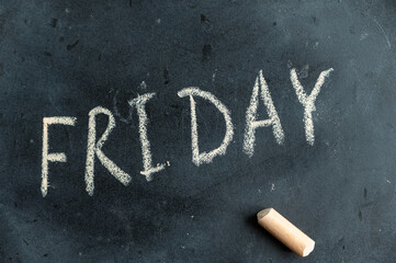 Friday. Name of the day of the week written in yellow chalk on black chalkboard. Handwritten text. A piece of colored chalk lies next to it. - Powered by Adobe