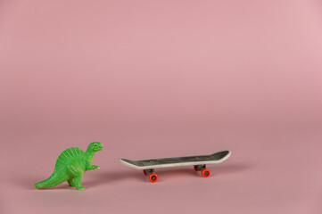 Miniature dinosaur standing next to a mini skateboard. Small green children's toy against a pink background. Close-up.  Selective focus.