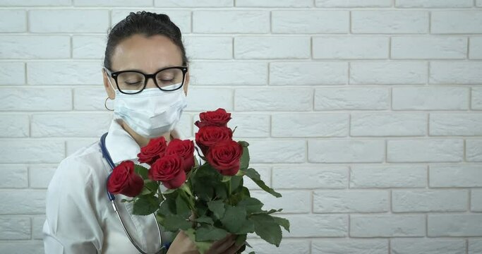Doctor in mask with flowers. A nice doctor in medical mask hold a bouquet with red flowers.