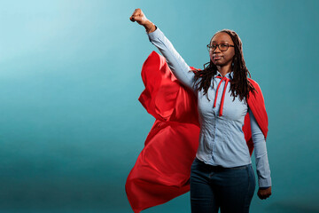 Brave and proud looking young adult superhero woman acting like a flying hero while wearing mighty...