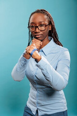 Defensive young adult person in self defense pose when encountering a life threat. Serious and brave woman getting in ready position for boxing while clenching fists with strength on blue background