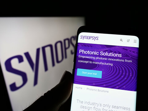 Stuttgart, Germany - 05-22-2022: Person holding cellphone with webpage of US technology company Synopsys Inc. on screen in front of logo. Focus on center of phone display.