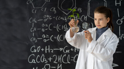 Young girl studies small plant in elementary science class. student holding magnifying glass. Earth day holiday concept. World Environment Day. Educational