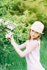 Fototapeta premium cute little girl with hat smiling in a blossoming apple orchard