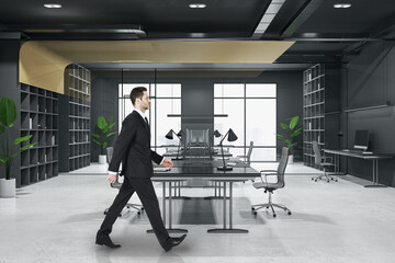 Obraz premium Attractive thoughtful young european business person walking in wooden and concrete office interior with furnituire and window with city view. CEO, executive and consulting concept.