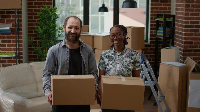 Portrait of husband and african american wife moving in together in new rented apartment flat. Holding cardboard boxes to unpack and prepare real estate property for relocation, household mortgage.