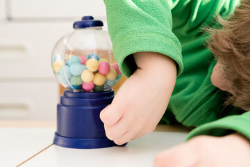 Beautiful boy plays with candy machine. Gumball Machine toy with colorful balls. Sweet childhood...