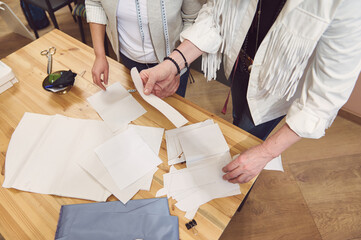 Top view of sewing patterns and blue fabric on a desk and two seamstresses work on creating new garment in fashion design studio and tailoring atelier