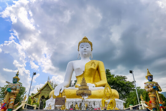 Beautiful big buddha image with rain cloud sky at Wat Phra That Doi Kham. Chiang Mai, Thailand.