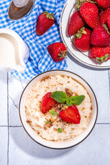 Rice porridge or pudding with fresh strawberry and nuts for breakfast, with plate of strawberries, white tiled background copy space