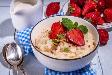 Rice porridge or pudding with fresh strawberry and nuts for breakfast, with plate of strawberries, white tiled background copy space