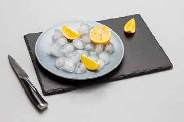 Melted ice and lemon slices on gray plate and on black stone board.