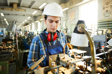 Serious busy skilled lady employee of industrial factory examining equipment while working on lathe...