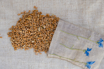 Pour out the wheat from a bag on a hemp canvas. The bag is decorated with embroidered cornflowers.