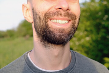 Fototapeta premium close-up part of the face, bearded young man 30 years old in bright rays of light, smiles charismatically, green fields in background, healthy lifestyle, Suburban and Rural, nature protection