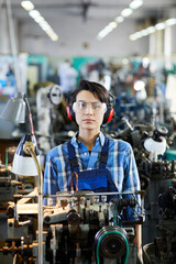 Serious gritty factory girl in workwear and safety goggles standing at lathe milling machine and...