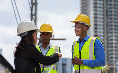 black engineer with glasses wear helmet, listen job detail from businesswoman. group of engineer working at construction site outside building in city