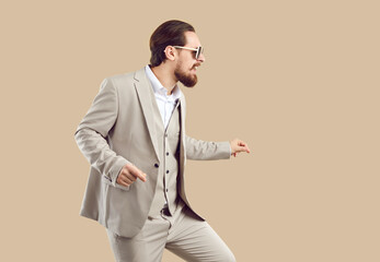 Happy cheerful man in suit and sunglasses having fun at party, dancing and beating rhythm by snapping fingers. Funny stealthy crafty guy walking on tiptoes. Side profile view. Music, fashion concept